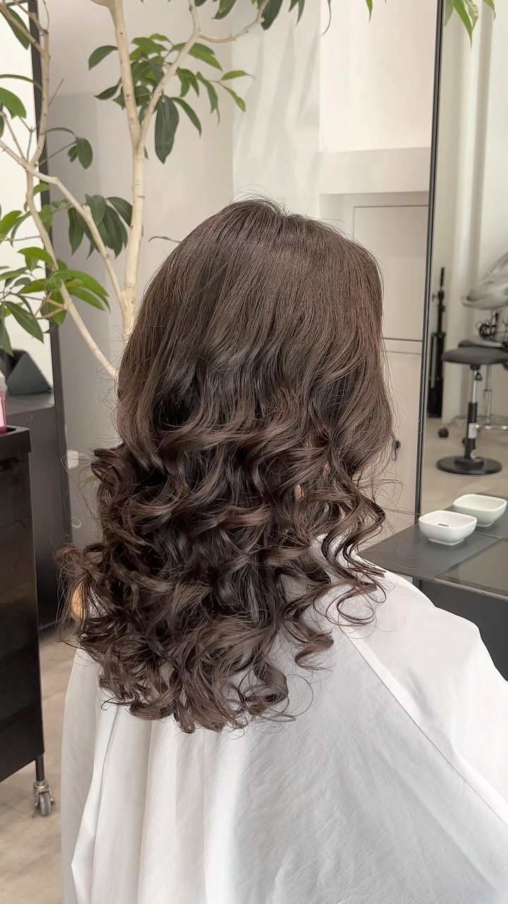 アッシュブラウンのロングヘアに柔らかく重なる大きなカールをかけた後ろ姿